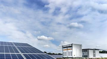 A photo of a PV panel and what appears to be a large industrual battery installation